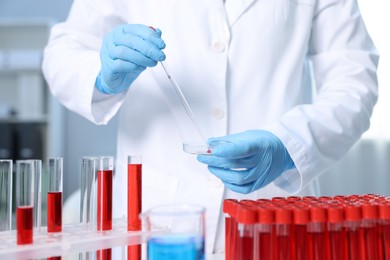 Laboratory testing. Doctor dripping blood sample into Petri dish indoors, closeup