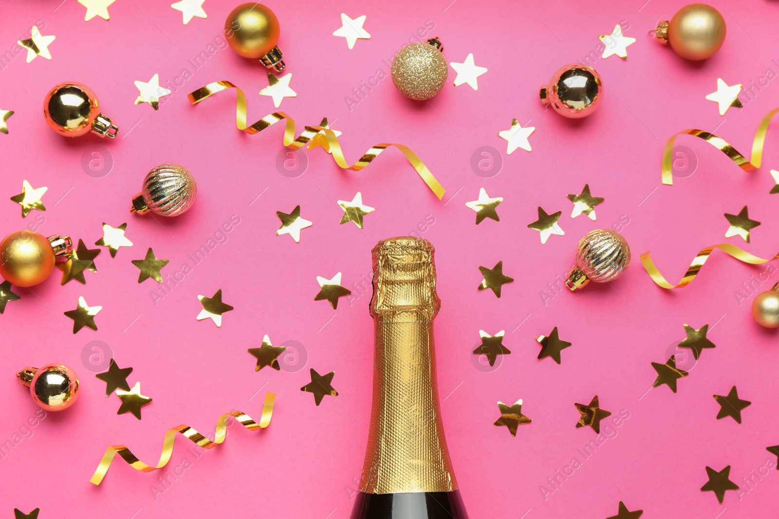 Photo of Bottle of sparkling wine, confetti and Christmas balls on pink background, flat lay