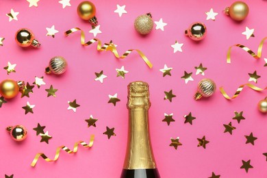 Photo of Bottle of sparkling wine, confetti and Christmas balls on pink background, flat lay