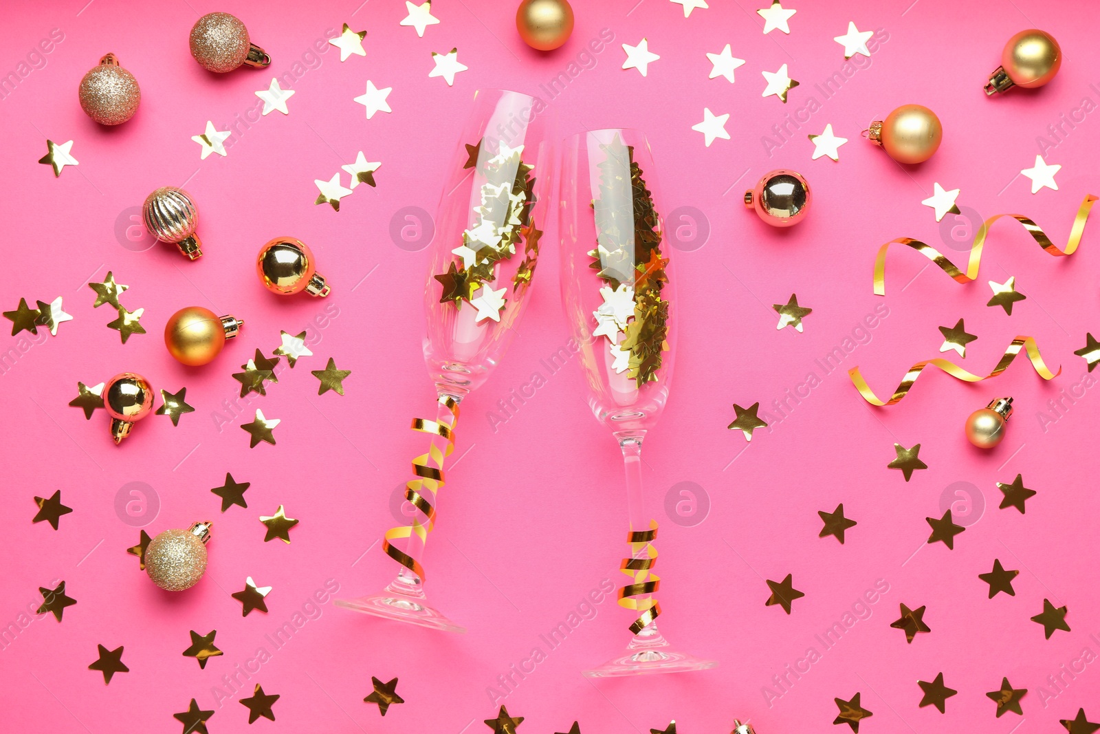 Photo of Wine glasses with confetti and Christmas balls on pink background, flat lay