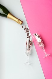 Photo of Glasses with confetti and bottle of sparkling wine on pink background, flat lay. Christmas decor