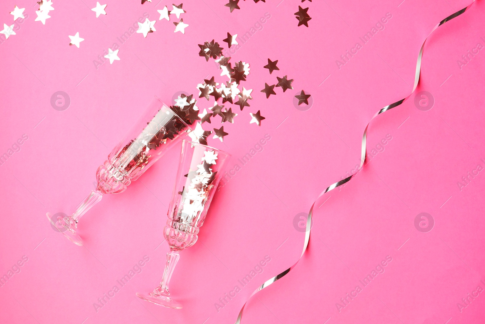 Photo of Wine glasses with confetti on pink background, flat lay. Christmas decor