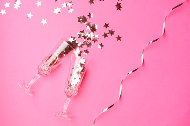 Photo of Wine glasses with confetti on pink background, flat lay. Christmas decor