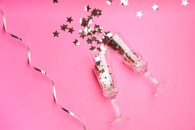 Photo of Wine glasses with confetti on pink background, flat lay. Christmas decor