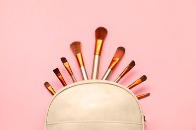 Photo of Cosmetic bag with makeup brushes on pink background, top view