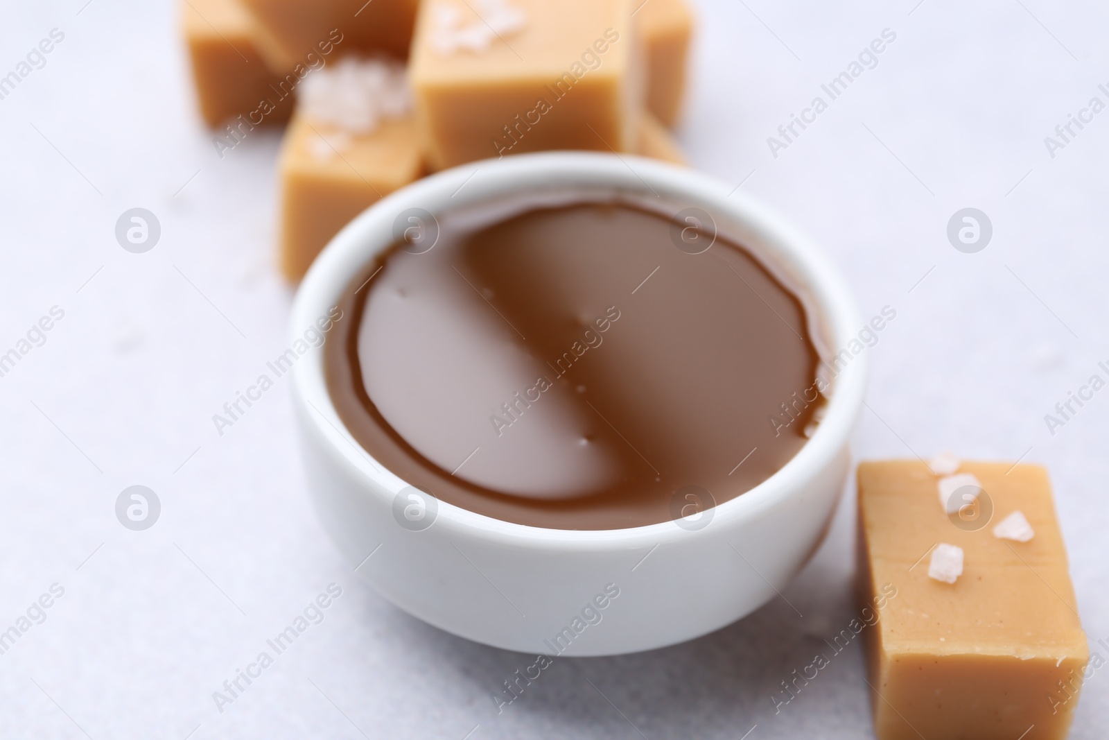 Photo of Tasty salted caramel in bowl and candies on light grey table, closeup