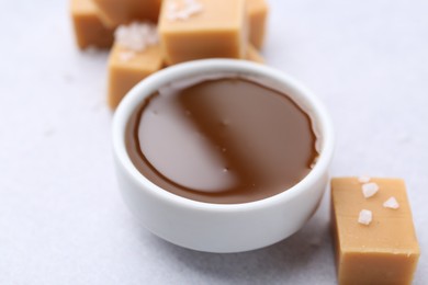 Photo of Tasty salted caramel in bowl and candies on light grey table, closeup