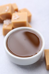 Photo of Tasty salted caramel in bowl and candies on light grey table, closeup