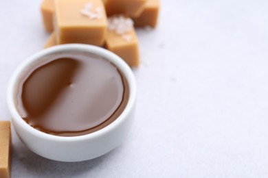 Photo of Tasty salted caramel in bowl and candies on light grey table, closeup. Space for text