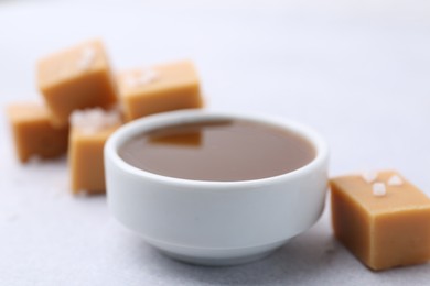 Photo of Tasty salted caramel in bowl and candies on light grey table, closeup