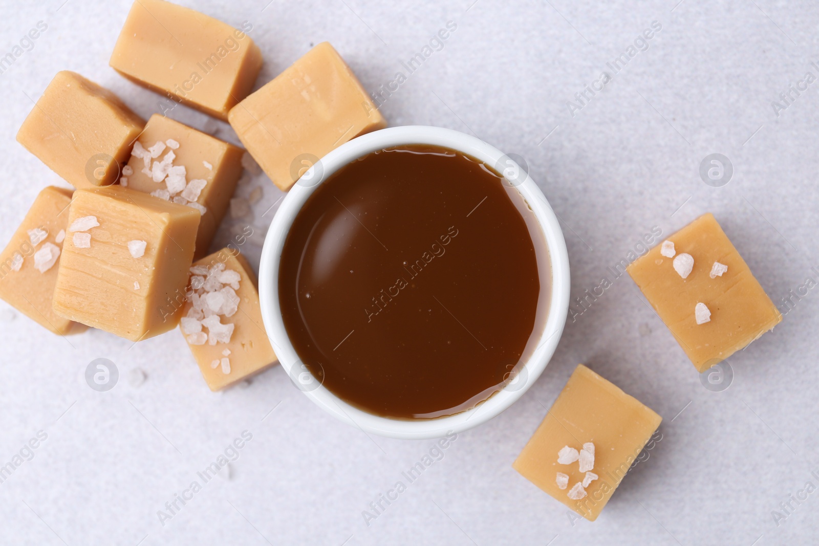 Photo of Tasty salted caramel in bowl and candies on light grey table, top view