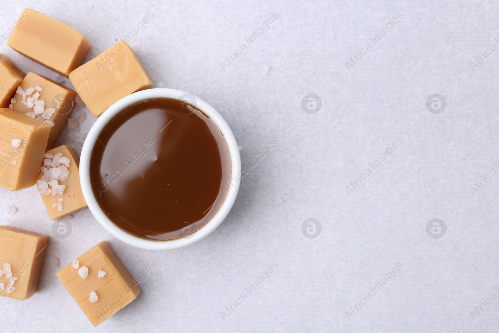 Photo of Tasty salted caramel in bowl and candies on light grey table, top view. Space for text