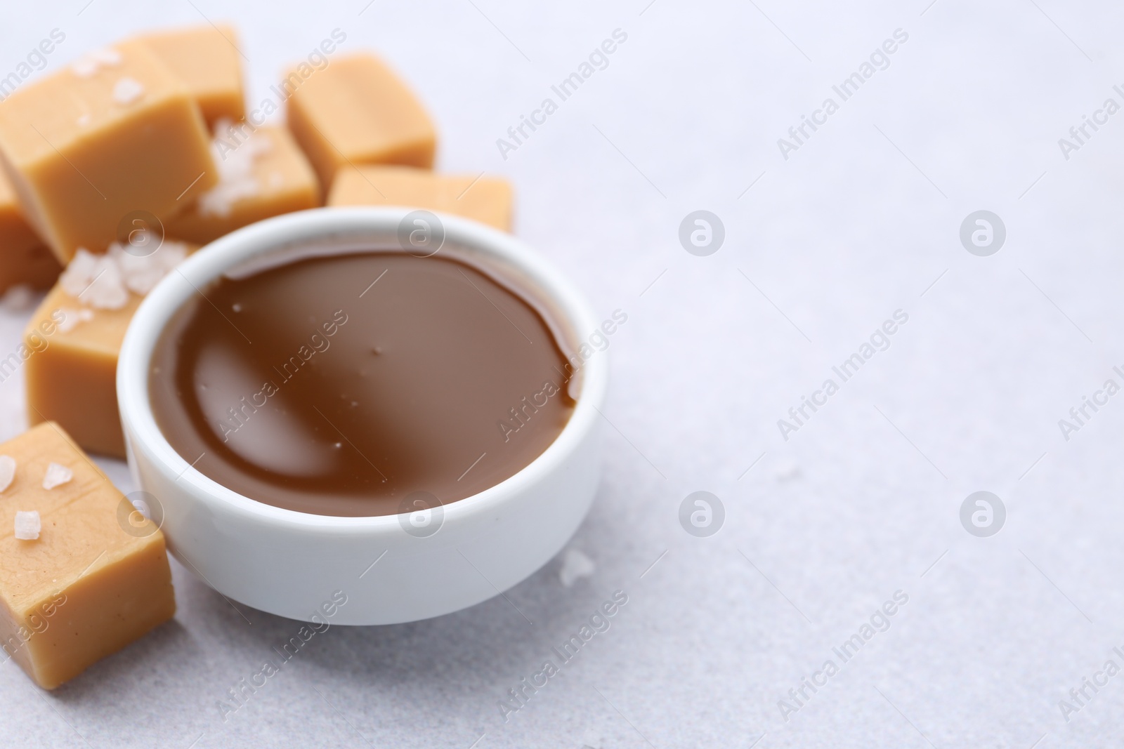 Photo of Tasty salted caramel in bowl and candies on light grey table, closeup. Space for text