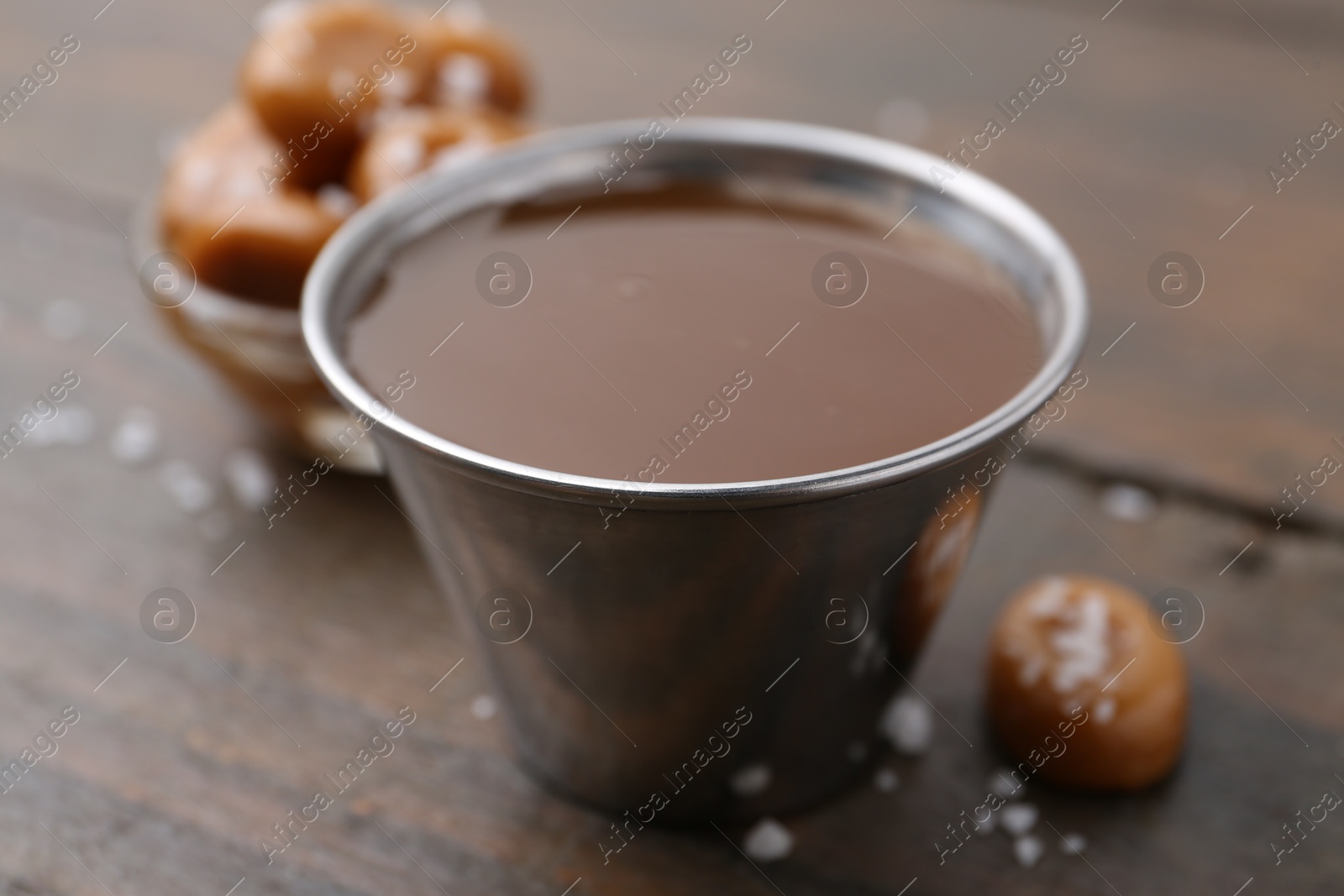 Photo of Tasty salted caramel in bowl and candies on wooden table, closeup