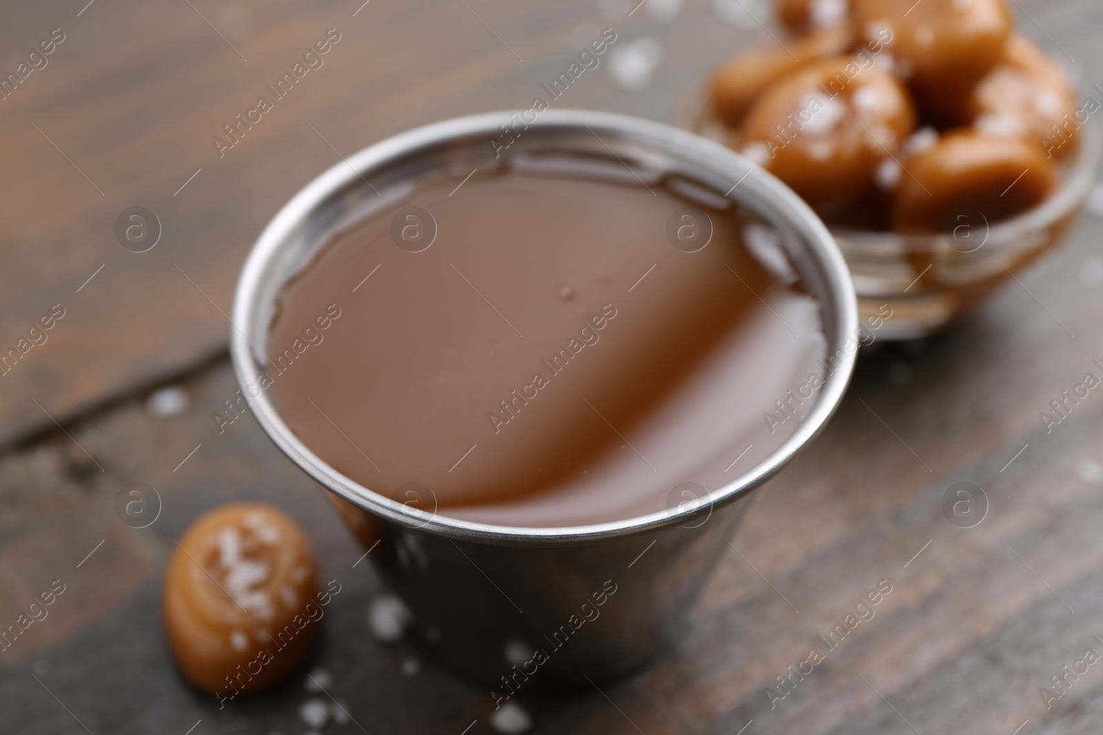 Photo of Tasty salted caramel in bowl and candies on wooden table, closeup