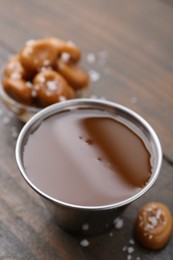 Photo of Tasty salted caramel in bowl and candies on wooden table, closeup