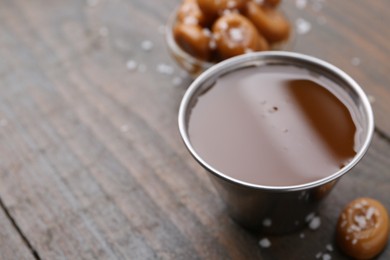 Photo of Tasty salted caramel in bowl and candies on wooden table, closeup. Space for text