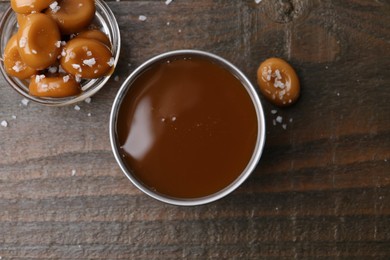 Photo of Tasty salted caramel in bowl and candies on wooden table, top view