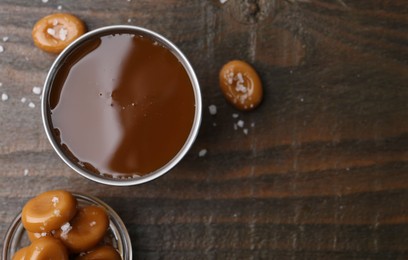 Photo of Tasty salted caramel in bowl and candies on wooden table, top view. Space for text