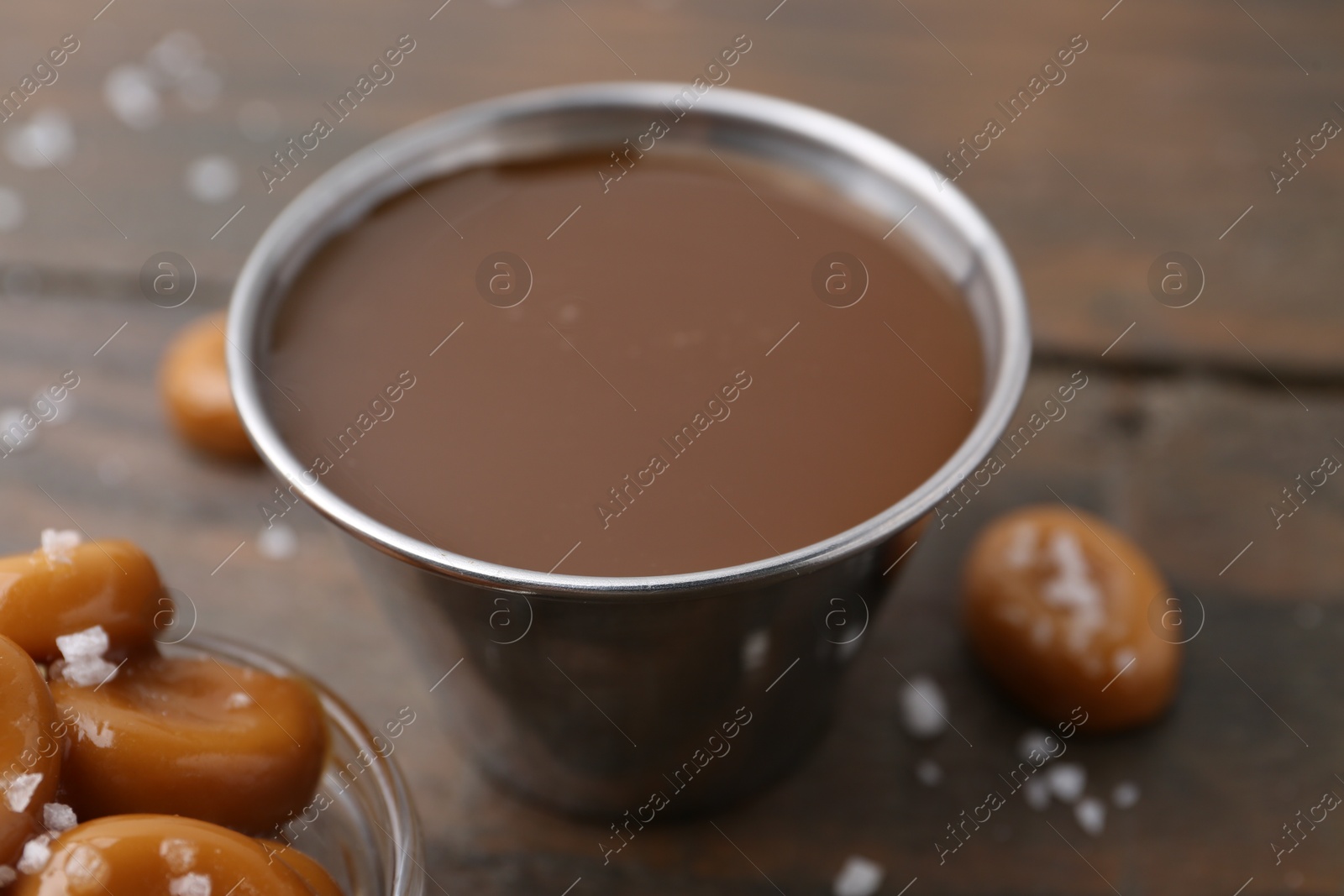 Photo of Tasty salted caramel in bowl and candies on wooden table, closeup