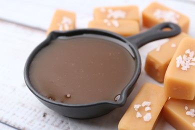 Photo of Tasty salted caramel in gravy boat and candies on table, closeup