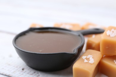 Photo of Tasty salted caramel in gravy boat and candies on table, closeup