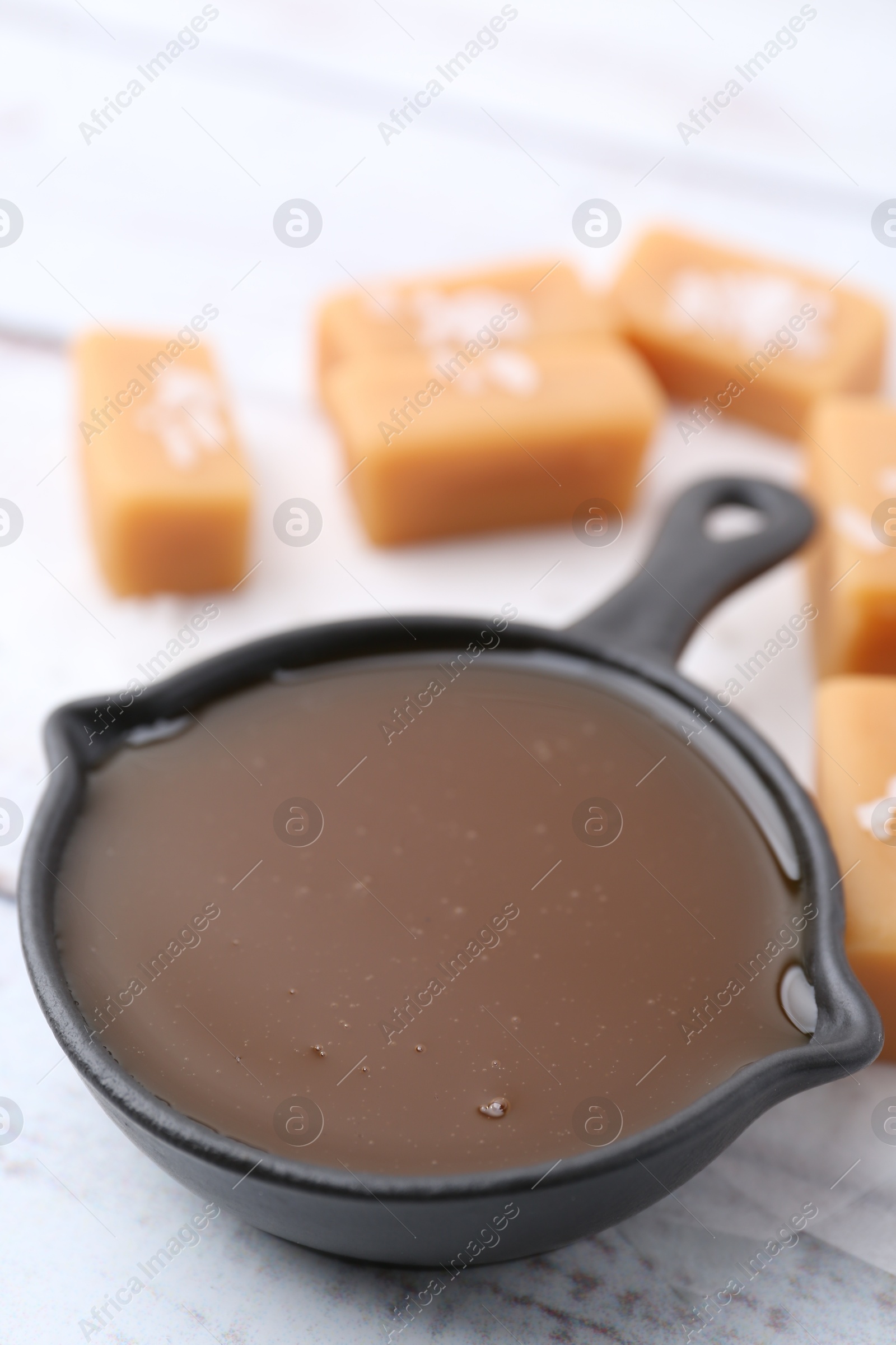 Photo of Tasty salted caramel in gravy boat and candies on table, closeup