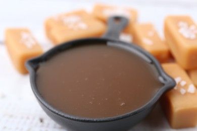 Photo of Tasty salted caramel in gravy boat and candies on table, closeup