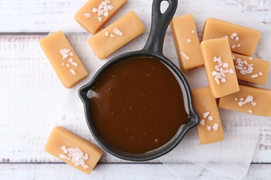 Photo of Tasty salted caramel in gravy boat and candies on white wooden table, top view