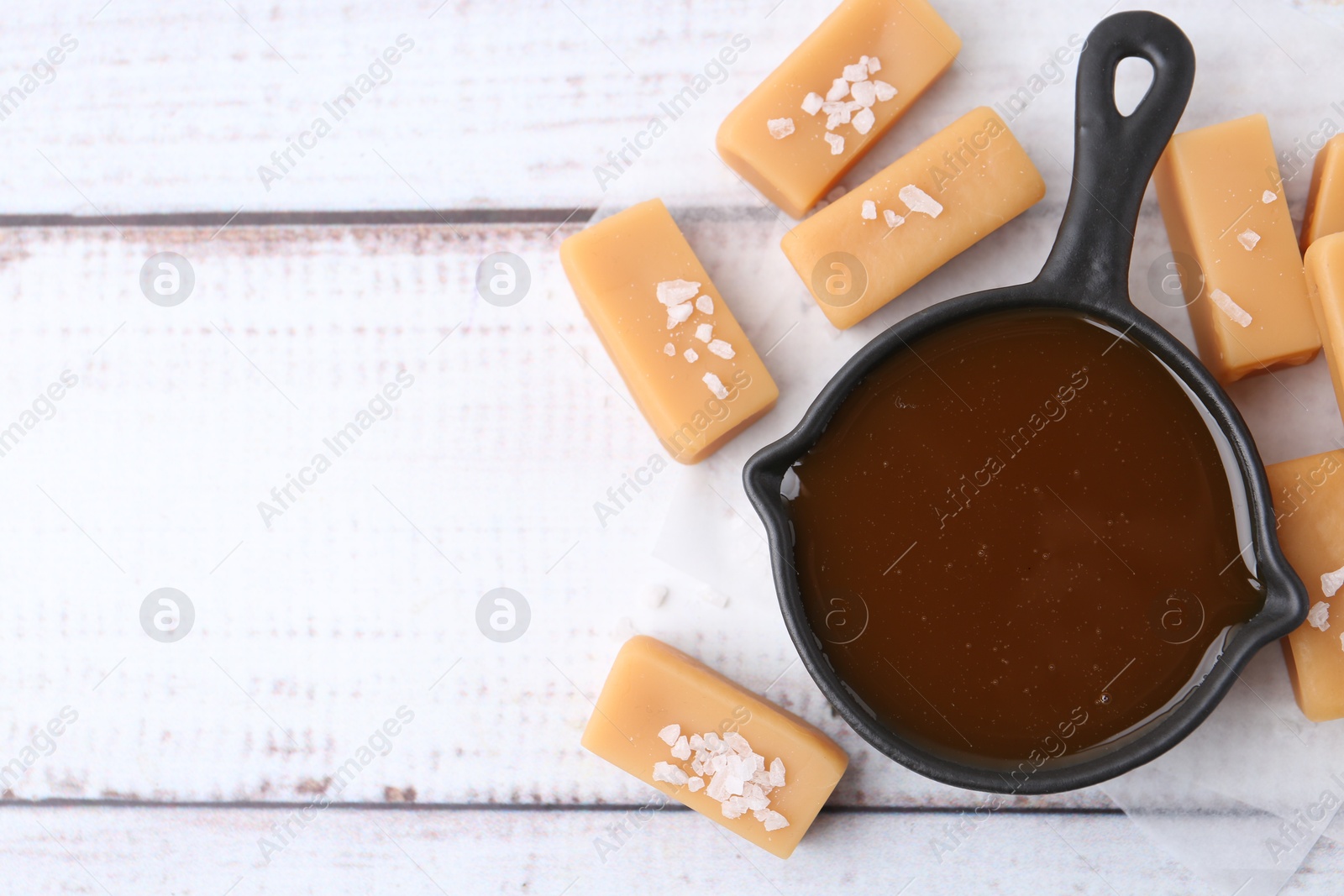 Photo of Tasty salted caramel in gravy boat and candies on white wooden table, top view. Space for text