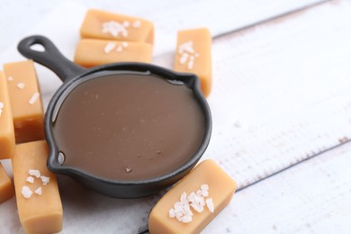 Photo of Tasty salted caramel in gravy boat and candies on white wooden table, closeup