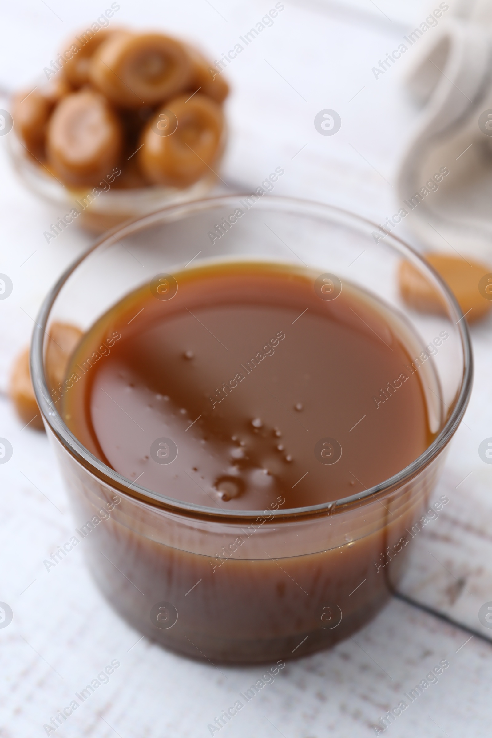 Photo of Tasty caramel sauce in bowl and candies on white wooden table, closeup