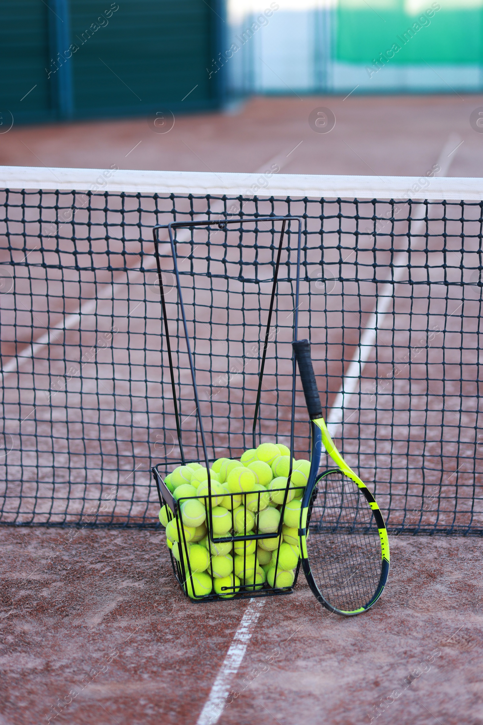 Photo of Tennis racket and balls in metal basket on court