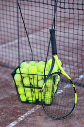 Tennis racket and balls in metal basket on court