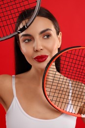 Beautiful young woman with tennis rackets on red background