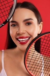 Portrait of beautiful young woman with tennis rackets on red background, closeup