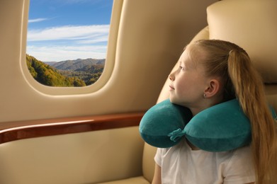 Little girl looking at mountains from airplane window