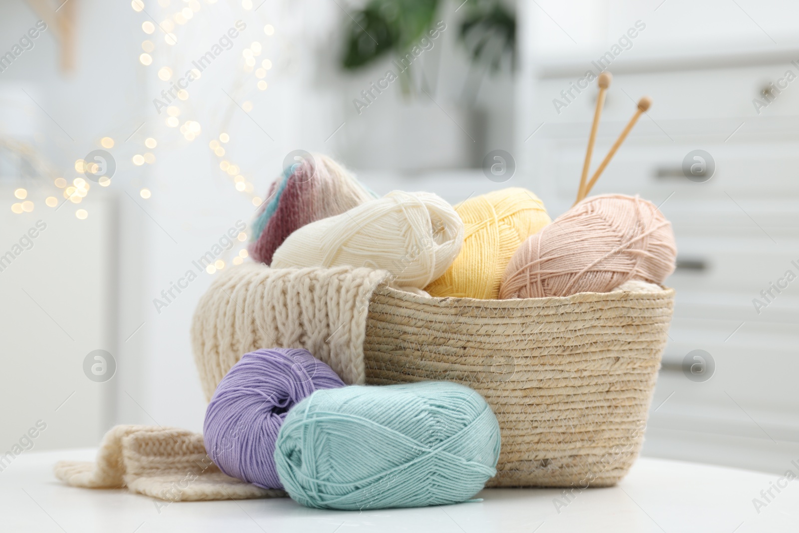 Photo of Skeins of yarn, knitting sample and needles on white table indoors