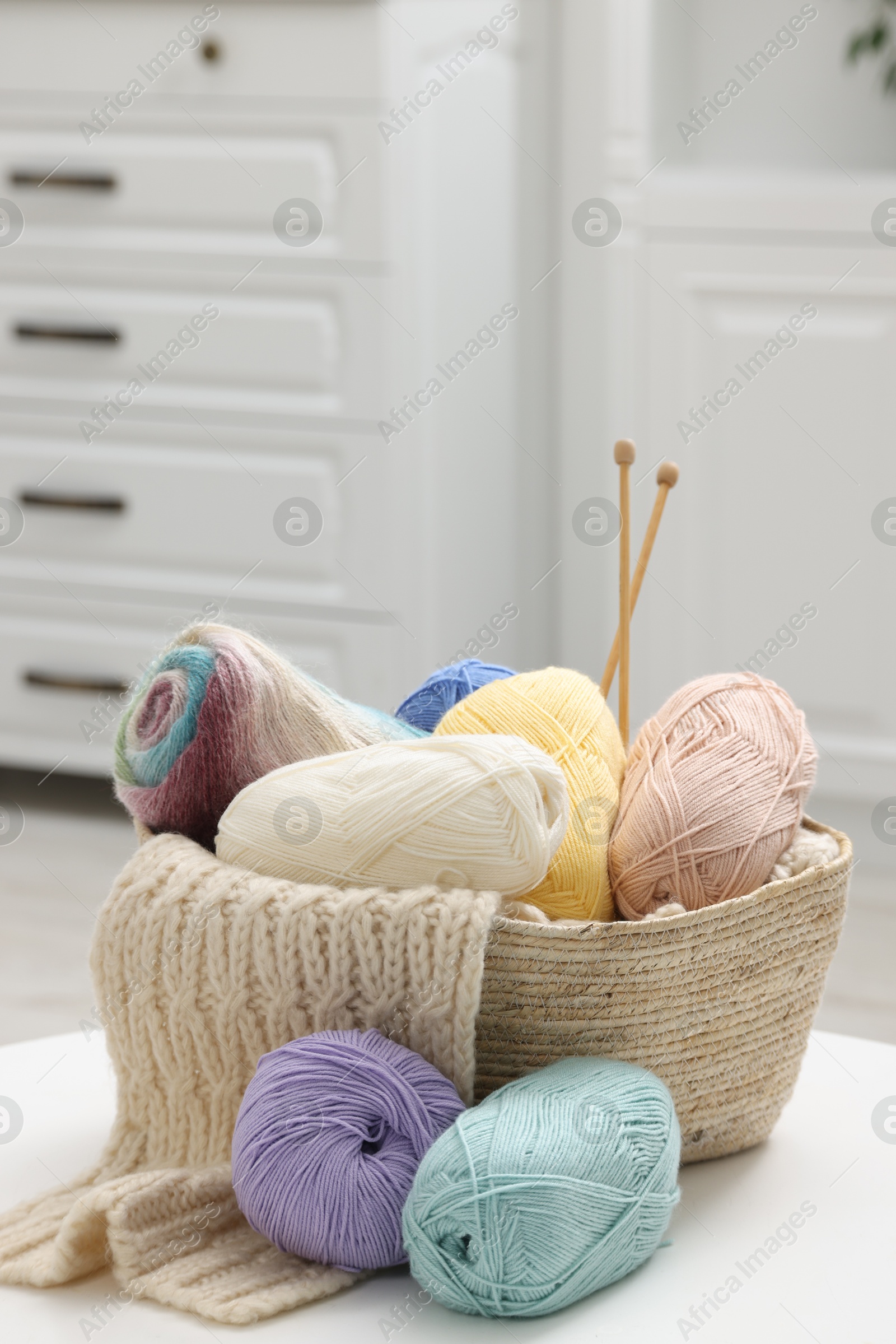 Photo of Skeins of yarn, knitting sample and needles on white table indoors