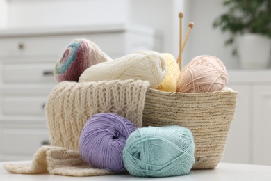 Skeins of yarn, knitting sample and needles on white table indoors