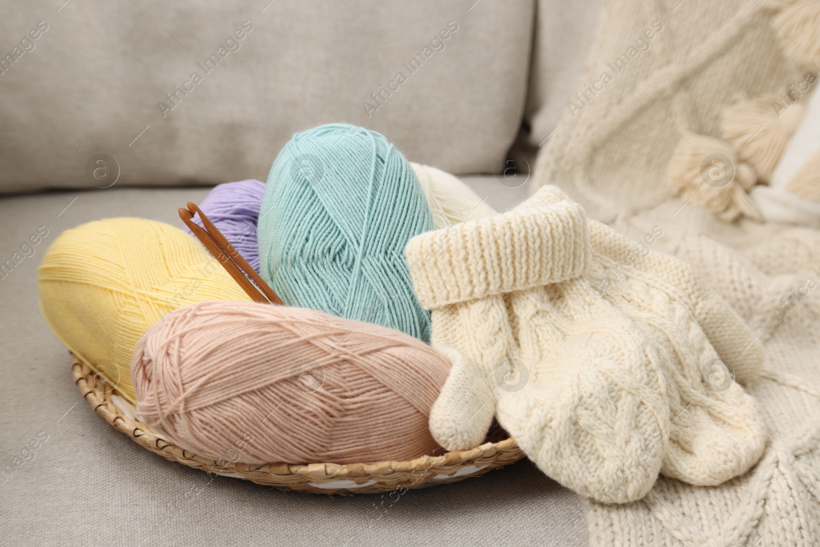 Photo of Skeins of soft yarn, crochet hooks and mittens on sofa