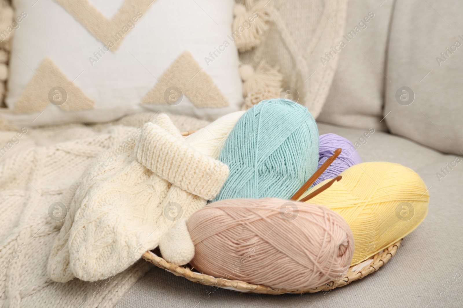 Photo of Skeins of soft yarn, crochet hooks and mittens on sofa