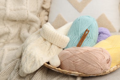 Skeins of soft yarn, crochet hooks and mittens on sofa