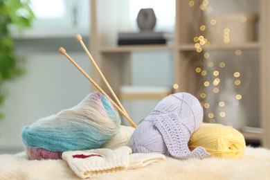 Photo of Skeins of yarn, needles and knitting sample on soft surface indoors