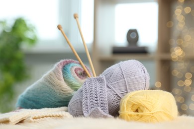 Skeins of yarn, needles and knitting sample on soft surface indoors, closeup