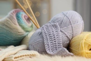 Photo of Skeins of yarn, mittens and knitting sample on soft surface, closeup