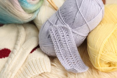 Photo of Skeins of yarn, mittens and knitting sample on soft surface, closeup