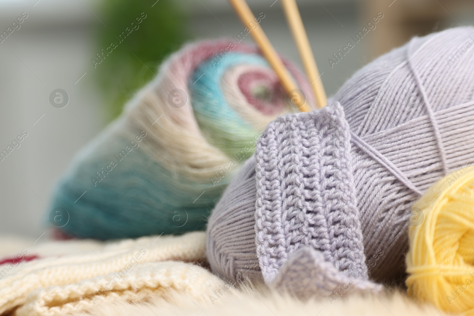 Photo of Skeins of yarn and knitting sample on soft surface indoors, closeup