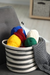 Skeins of soft yarn, knitting sample and needles on armchair indoors