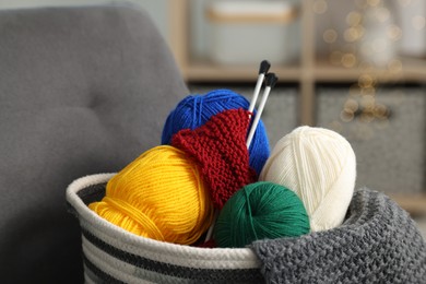 Photo of Skeins of soft yarn, knitting sample and needles on armchair indoors